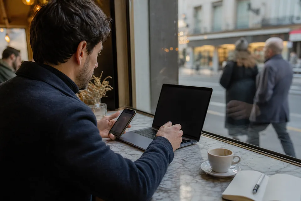 A creator comparing two dashboards on a laptop and a phone at a cafe table