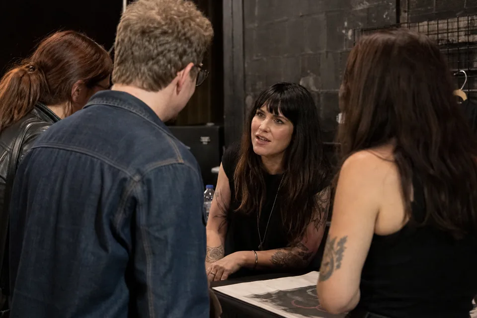 A singer chatting with fans at a merch table after a small concert