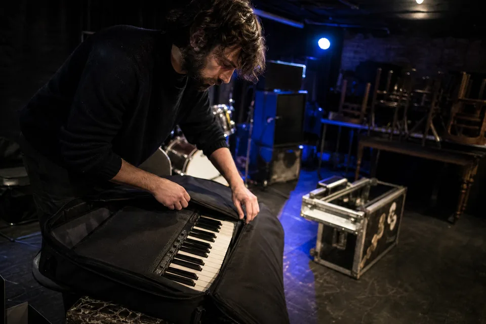 A musician packing a keyboard into a case after a gig in an empty venue